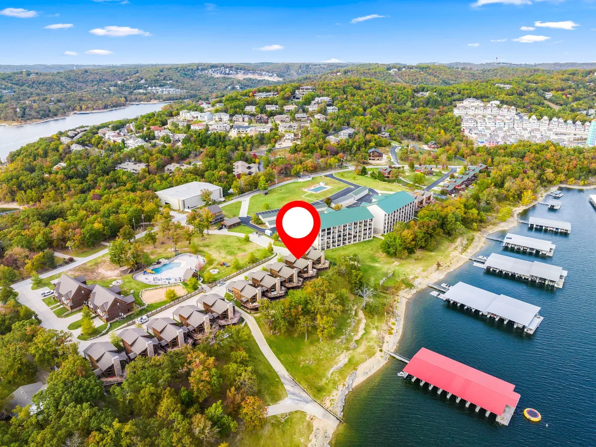 A stunning lakefront view with lush green trees, modern resort buildings, and a dock with boats moored in the water. The scene captures the serenity and recreational spirit of the lakeshore, with the sun setting over Table Rock Lake and hints of water sports and summer activities unfolding.