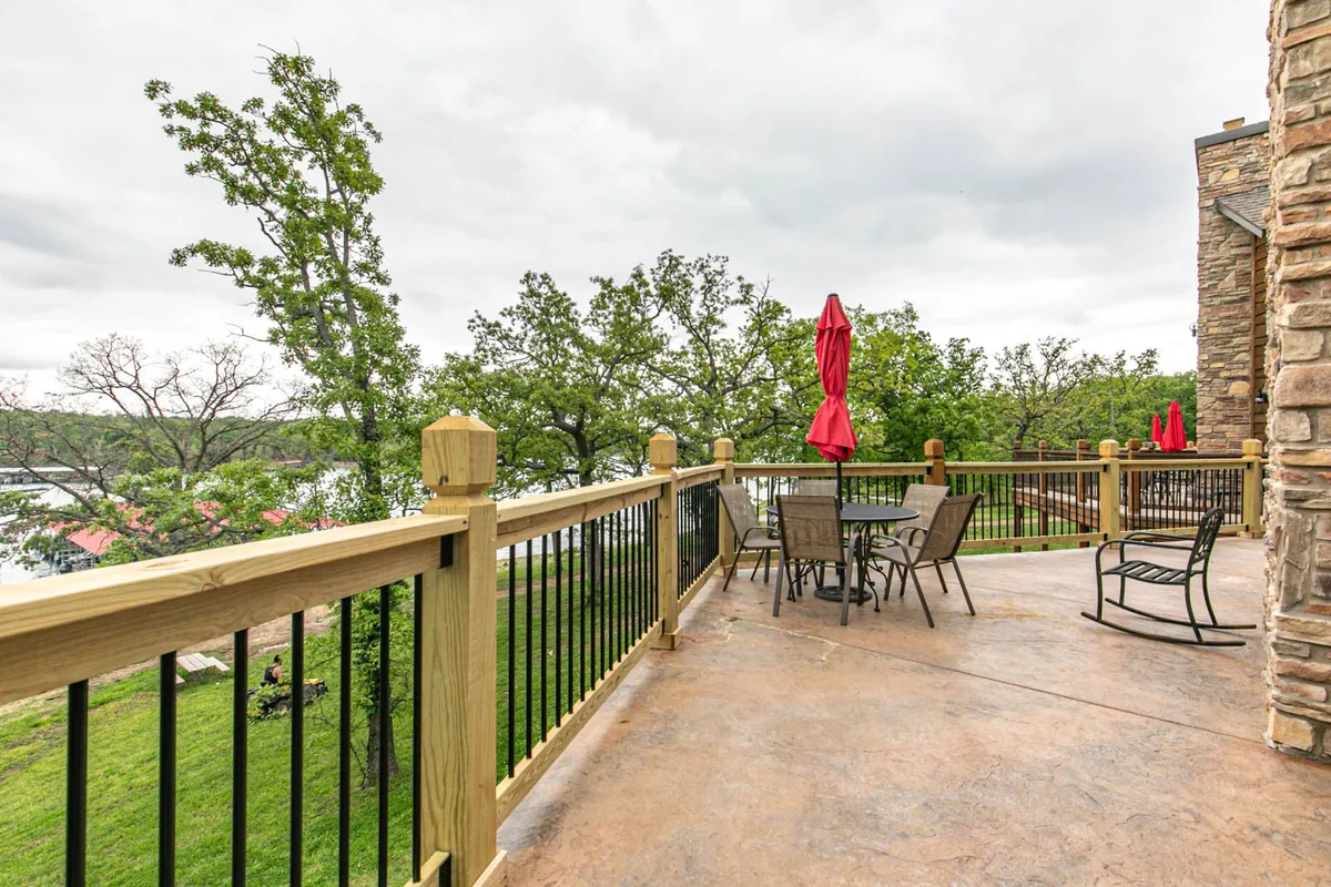This exterior image captures a welcoming patio area furnished with comfortable seating and red umbrellas. The patio overlooks a tranquil lake surrounded by green trees, with plenty of open space for social gatherings and celebrations. The view suggests the perfect spot for enjoying sunset views or relaxing with loved ones outdoors.