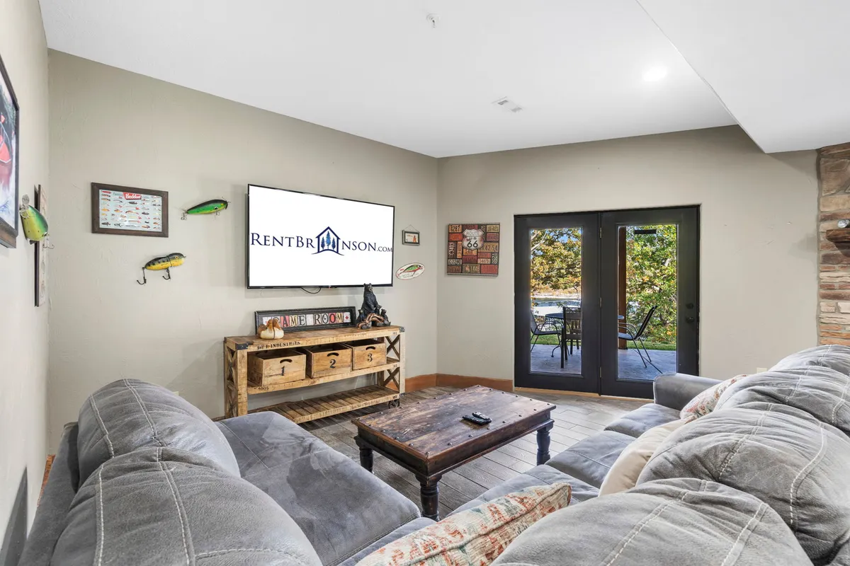A modern family room with a large grey sectional sofa arranged around a wooden coffee table and facing a flat-screen TV, with sliding glass doors leading directly to an outdoor patio.