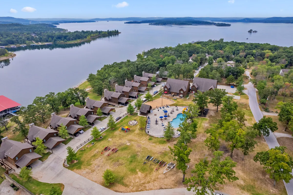This exterior image captures a lakeside scene featuring a sparkling swimming pool, nearby cabins, and lush greenery. The serene lake is visible in the background, with open spaces that invite various outdoor activities. The setting reflects both summer fun and the tranquility of fall and spring.