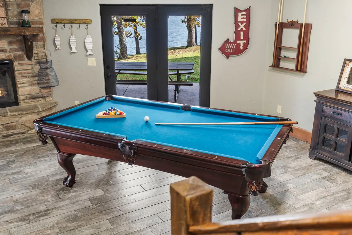 This interior shot features a pool table near a cozy fireplace, with double doors opening to a scenic outdoor view of the lake. The space exudes a casual, entertaining atmosphere, ideal for friendly game nights or relaxed evenings shared with friends and family.