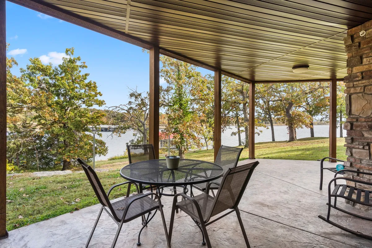 An exterior patio table is set among mature trees with a calming water view just beyond. The tranquil mood suggests peaceful mornings, sunset reflections, or cozy autumn afternoons spent outside, soaking up nature in different seasons.