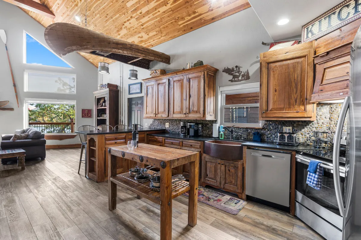 A view of the kitchen space featuring a rustic wooden kitchen island, large windows with scenic views, and cabinetry with wooden beams overhead. The layout invites family gatherings and socializing while preparing meals, echoing the communal atmosphere described for the kitchen and dining area.