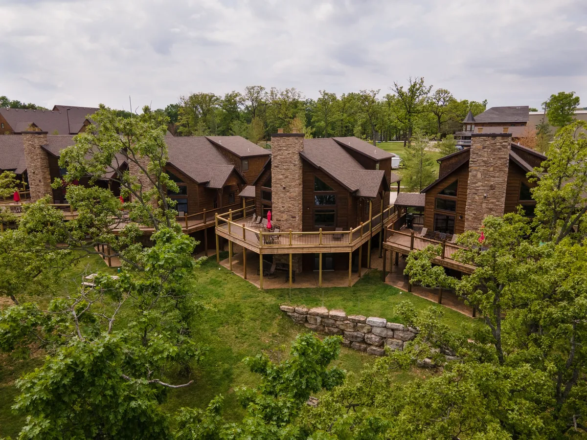 This exterior image features a welcoming wooden deck with stone chimneys and a backdrop of surrounding trees. The scene is tranquil and inviting, suggesting a perfect spot for relaxing outdoors and easily accessible for pet walks.
