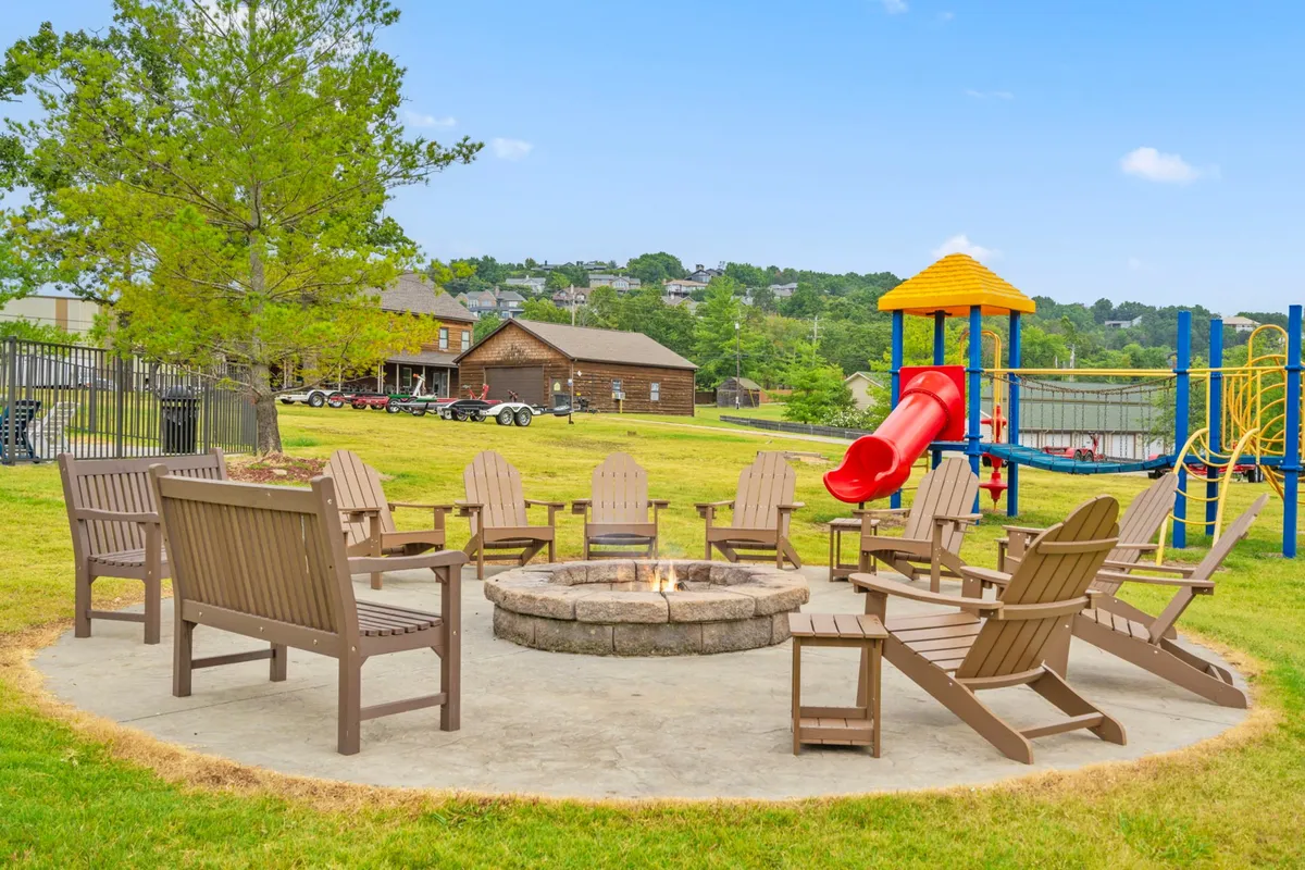 A relaxed communal area at the resort featuring a fire pit surrounded by Adirondack chairs and a nearby playground with a slide. Children are playing energetically while adults gather around the fire, enjoying conversation and the evening atmosphere.