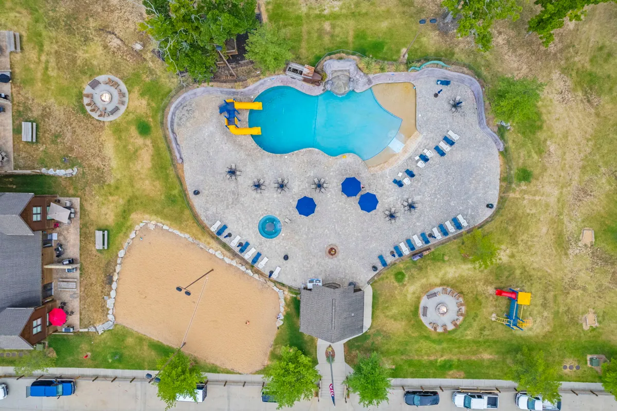 This lively exterior image captures the resort's swimming pool area, complete with water slides, a sand volleyball court, lounge chairs, a hot tub, and a nearby fire pit. The scene is filled with guests enjoying a range of activities from swimming and sunbathing to playing volleyball and gathering for barbecues.