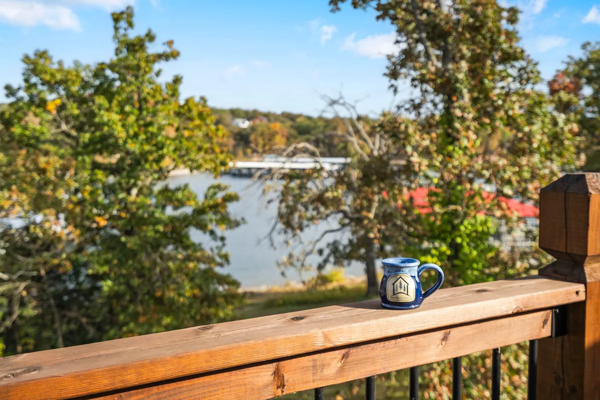 The wrap-around porch with a coffee mug resting on the railing, surrounded by trees and offering a tranquil water view. The scene suggests peaceful mornings and serene moments spent watching the sunrise over Table Rock Lake.